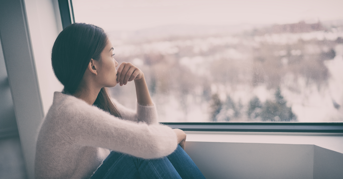 Woman sadly looking out of window at winter landscape