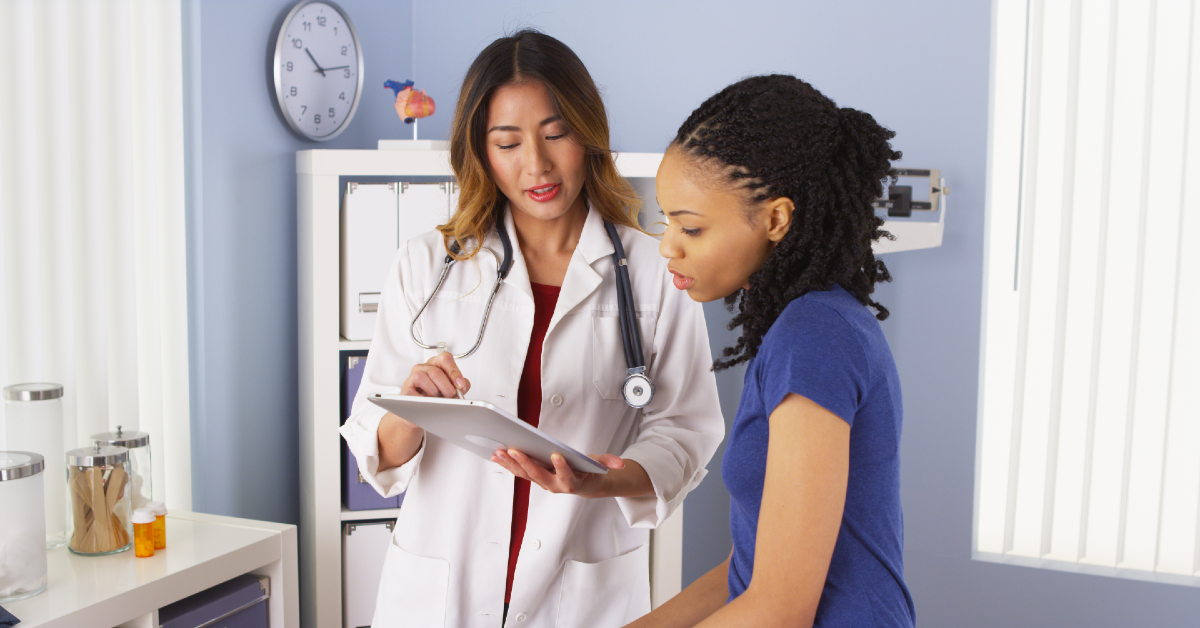 Asian doctor showing African American patient information on a tablet